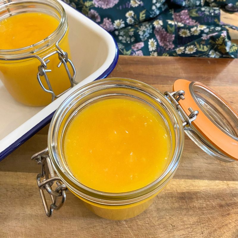 Jar of homemade lemon curd on a wooden board, with a floral cloth in the background - lemon curd recipe NZ