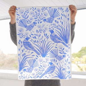 Person holding the 100%NZ Birdsong Blues  Tea Towel showing a blue bird and foliage print.