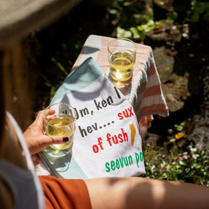 100%NZ Fush & Chups tea towel folded on  bench with drinks.