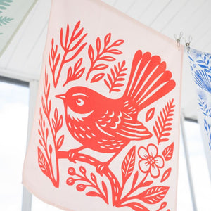 100%NZ Woodcut Fantail Tea Towel pegged to a clothes line hanging outside under cover.