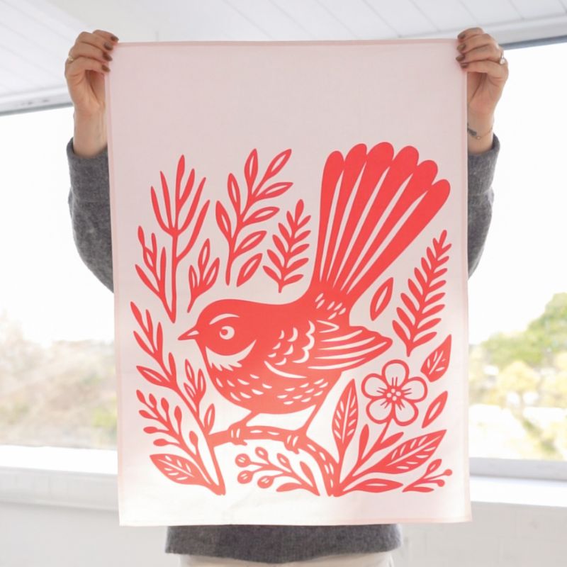 100%NZ Woodcut Fantail Tea Towel pegged to a line, shown against a white background.