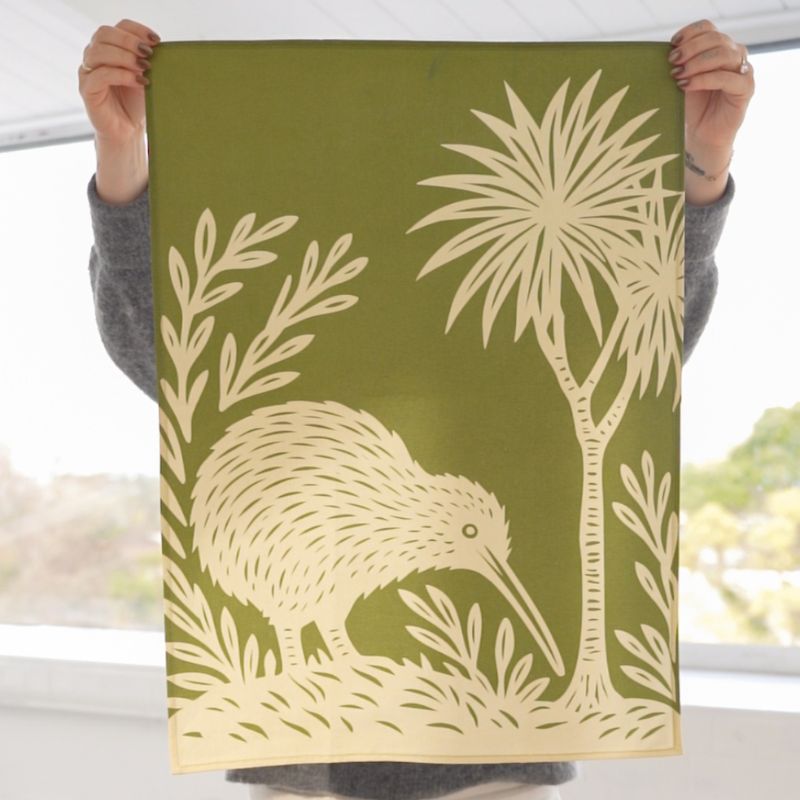 100%NZ Woodcut Kiwi Tea Towel shown pegged to a line against a white background.
