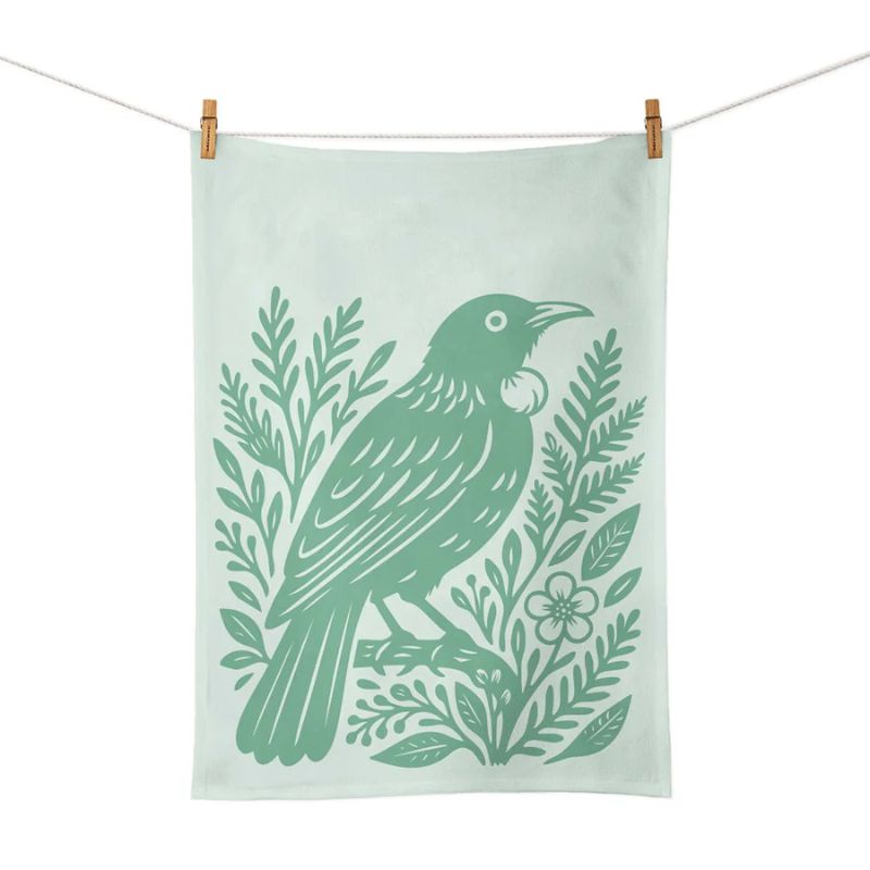 100%NZ Woodcut Tūī Tea Towel shown pegged from a line on a white background. 