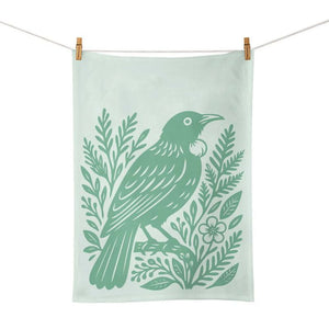 100%NZ Woodcut Tūī Tea Towel shown pegged from a line on a white background. 