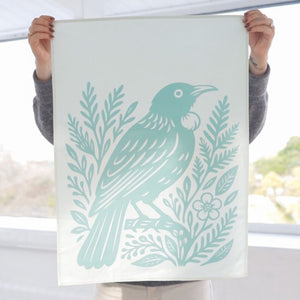 Person holding 100%NZ Woodcut Tūī Tea Towel with a green bird and leaf design.