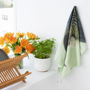 100%NZ Hushed Green Tūī Tea Towel hanging in a kitchen.