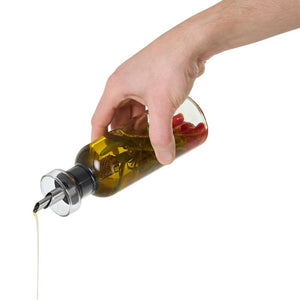 Hand pouring olive oil from a glass oil bottle dispenser - oil infused with herbs and spices.