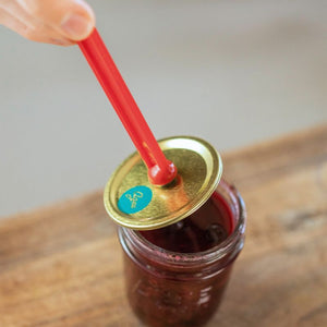 Agee magnetic lid lifter being used to place a gold Agee lid onto a jar of jam.