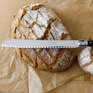 Loaf of bread with the André Verdier Laguiole Debutant Bread Knife with black handle on brown paper