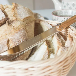 André Verdier Laguiole Debutant Bread Knife – Country, resting in a woven basket filled with sliced bread.