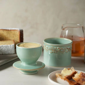 Antique Sea Spray Butter Bell Crock displayed open with a slice of cake and herbal tea in the background