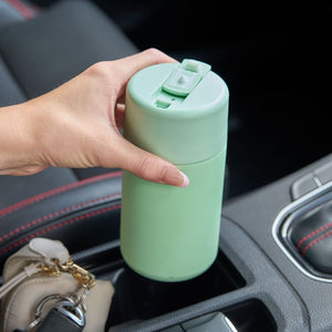 Hand holding the Avanti Brew Insulated Travel Cup in Soft Mint in a car's cup holder.
