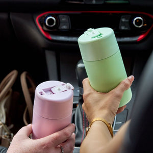 Two hands holding the Avanti Brew Insulated Travel Cups in lilac and a green inside a car.
