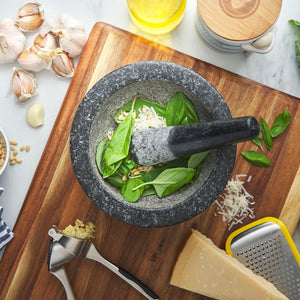 Avanti Low Profile Mortar & Pestle in Black with basil leaves on a wooden cutting board, surrounded by garlic, oil, and cheese.