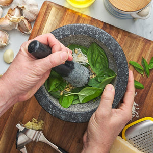 Person using the Avanti Low Profile Mortar & Pestle in Black with herbs on a wooden cutting board