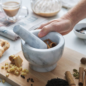 Avanti Marble Footed Mortar & Pestle in white styled next to herbs and spices with person holding onto the side.