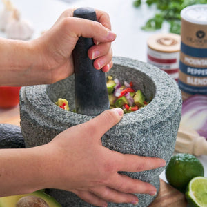 Person using the 20 cm Avanti Rough Mortar & Pestle in grey with ingredients on a kitchen counter