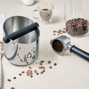 Avanti Stainless Steel Knock Box styled next to scattered coffee beans, a cup of coffee and a portafilter.