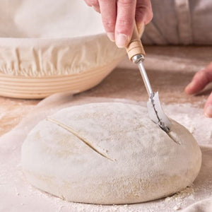 Person scoring a loaf of bread with the Bakemaster Bread Lame on a floured surface.