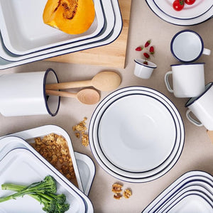 Set of white Bakemaster enamelware with blue rims on a wooden surface with food items.