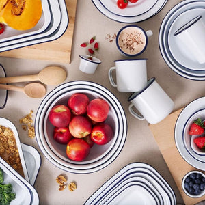 Bakemaster enamelware on a table setting with fruit and wooden spoons on a beige surface