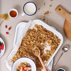 Baked granola Bakemaster Enamel Baking Tray with a spoon, berries, and milk on a beige surface.