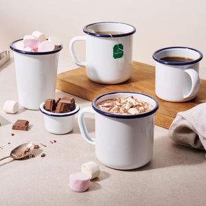 Bakemaster Enamel Mugs on a wooden board, filled with hot chocolate and tea, surrounded by marshmallows, chocolate pieces, and a spoon.