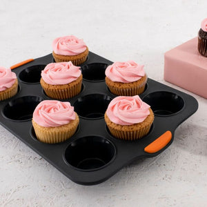 Bakemaster Silicone Muffin Pan – 12 Cup shown holding several cupcakes with pink frosting on a light textured surface.