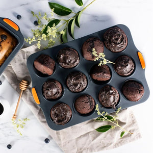 Bakemaster Silicone Muffin Pan – 12 Cup filled with chocolate chip muffins, styled on a light beige cloth over a white marble surface.