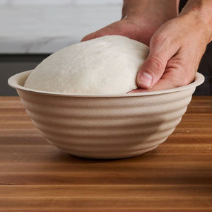 Person putting dough into the Brod & Taylor Boule Banneton on a wooden surface.