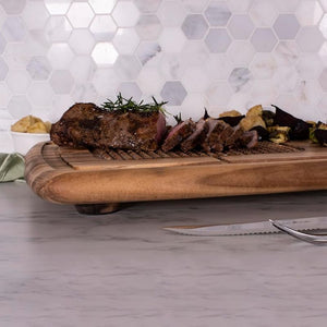 Acacia carving board in use with a cooked roast and carving knives placed beside.