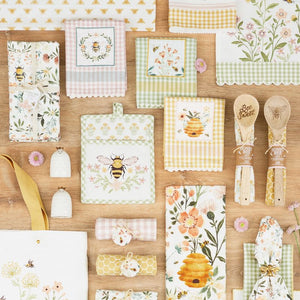 Design Imports Honey Bee collection of kitchen items with gingham, floral and bee designs on a wooden surface.