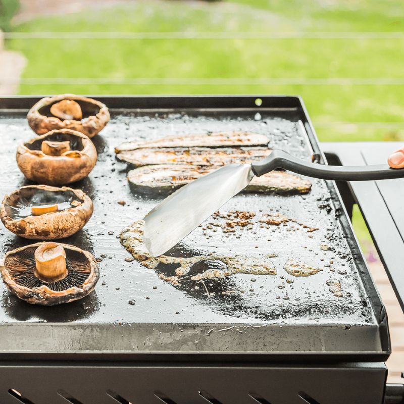 Dreamfarm BBQ Chopula scraping residue from a hot barbecue grill plate.