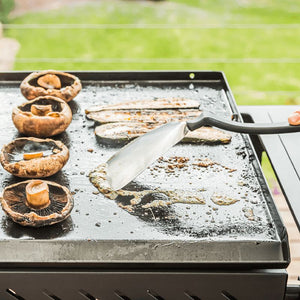 Dreamfarm BBQ Chopula scraping residue from a hot barbecue grill plate.