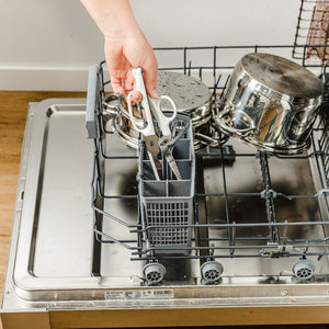 Hands placing Dreamfarm Bishears into dishwasher, scissor blades pulled apart for more effective washing.