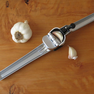 Dreamfarm Garject garlic press on a wooden board being used to press unpeeled garlic cloves - kitchen utensils NZ