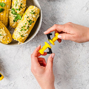 Hands pulling Dreamfarm Lockorns corn cob holders apart, shown near a bowl of corn.