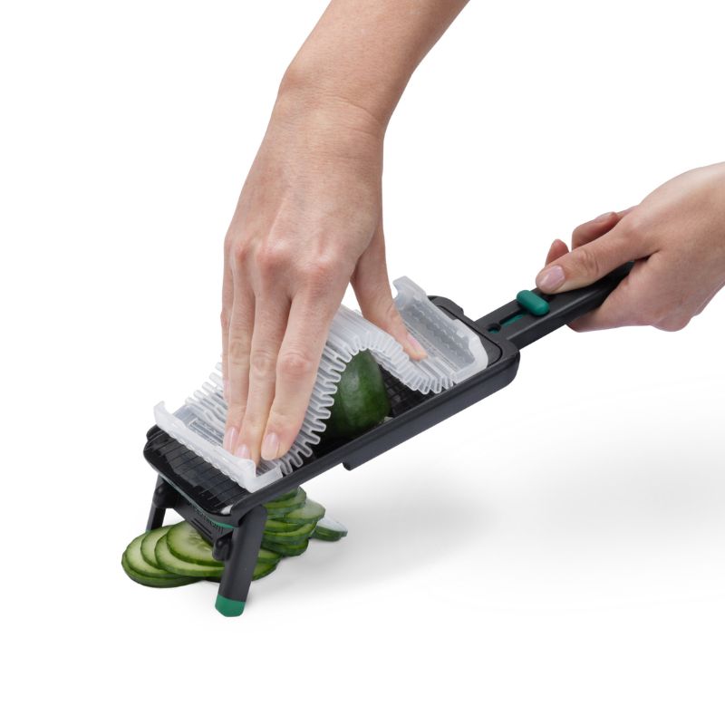 Dreamfarm Nocutu mandoline being used with safety hand guard to slice vegetables