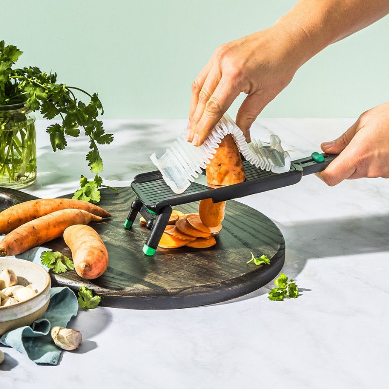 Dreamfarm Nocutu mandoline being used with safety hand guard to slice vegetables
