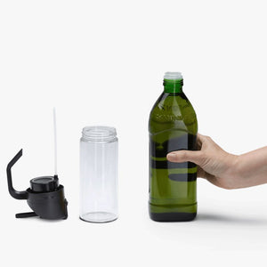 Person holding a bottle of oil next to the  Dreamfarm Oileroo on a white background.