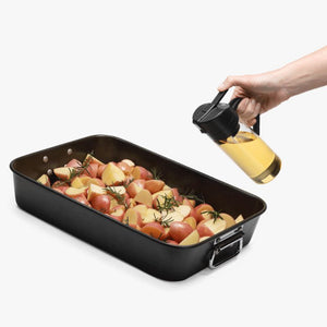 Person holding the Dreamfarm Oileroo – Oil Sprayer & Pourer above a tray of roast potatoes on a white background.