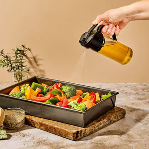 Person spraying oil onto roast vegetables with the Dreamfarm Oileroo