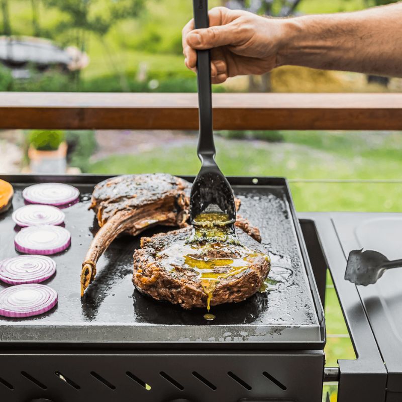 Dreamfarm BBQ spatula lifting grilled steak beside vegetables on barbecue grill.