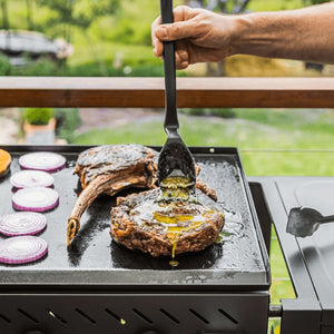 Dreamfarm BBQ spatula lifting grilled steak beside vegetables on barbecue grill.