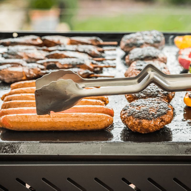 Dreamfarm BBQ tools flipping sausages and burger patties on a hot BBQ grill.