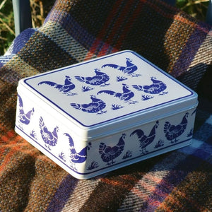 Emma Bridgewater Blue Hens Biscuit Tin shown on a rustic wool blanket outside.