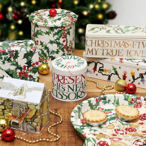 Collection of Emma Bridgewater Christmas-themed tins and trays on a wooden surface with a festive background.