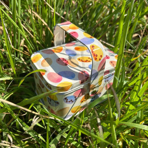 Emma Bridgewater Mini Eggs Easter Handle Basket placed in grass, showing colourful egg pattern.