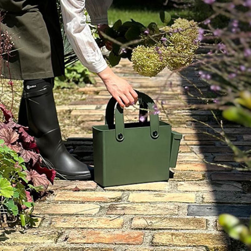 Woman holding flower cuttings bending to pick up the Hachiman Garden Tool Bag with Pocket