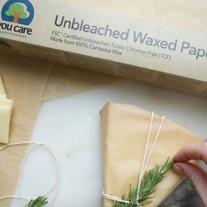 Unbleached waxed paper roll with a block of cheese and rosemary on a marble surface